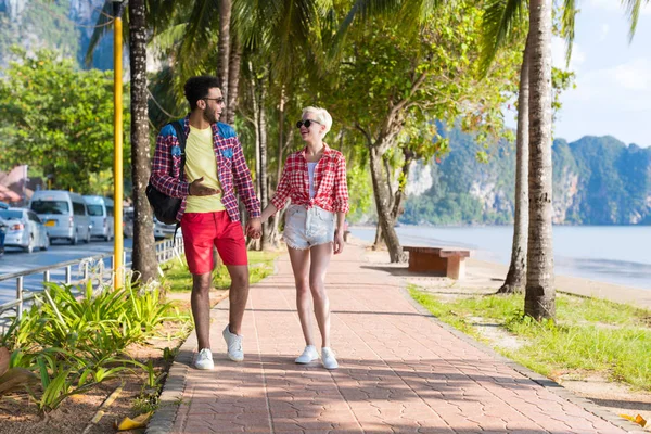 Pareja casual con las manos en la mano caminando en el parque de palmeras tropicales, hermosos jóvenes en vacaciones de verano —  Fotos de Stock