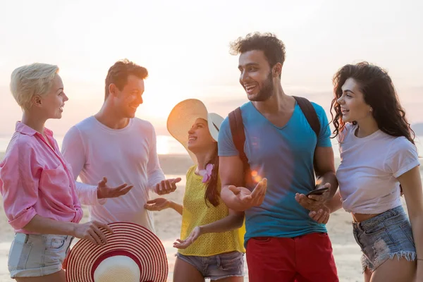 Skupina lidí na pláži při západu slunce mluví rádi, s úsměvem, Mix závod turisté sdělení o pobřežní — Stock fotografie