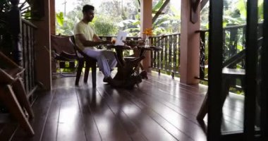 Genç adam kullanma dizüstü bilgisayar terasta oturan tablo açık havada İspanyol gülümseyen mutlu adam