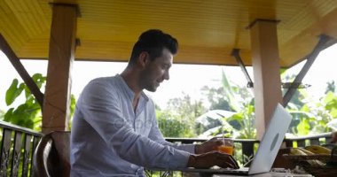 Laptop üzerinde yaz teras tropikal orman, açık havada bilgisayarda yazarken adam içecek suyu otelin kahvaltı sırasında çalıştığı genç iş adamı