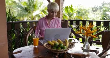Mutlu kadın yaz terasında kahvaltı sırasında dizüstü bilgisayarda Internet açık havada tarama genç güzel kadın tropikal ormanda yazarak