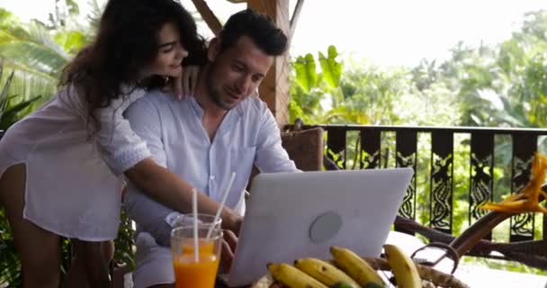 Les jeunes couples utilisent le coputer d'ordinateur portable ensemble sur la terrasse dans la forêt d'été, bel homme et femme surfant sur Internet parlant — Video
