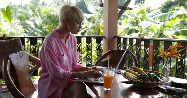 Молодая девушка использовать ноутбук компьютер, сидя за столом на летней террасе, красивая женщина болтает в Интернете на открытом воздухе — стоковое видео