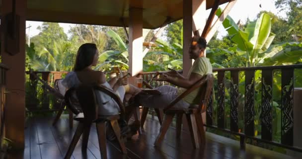 Pareja feliz sentada en la terraza al atardecer hablando, el joven y la mujer se comunican juntos bebiendo jugo — Vídeo de stock