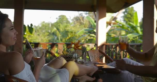 Pareja feliz relajándose en la terraza de verano al atardecer hablando, hombre joven y mujer descansando comunicándose juntos bebiendo jugo — Vídeo de stock