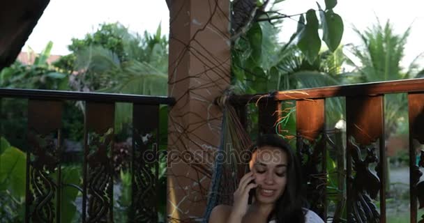Fiatal nő beszélgetés okostelefon Cell segítségével a nyári teraszon boldog mosolygó függőágyban fekvő telefonhívás — Stock videók