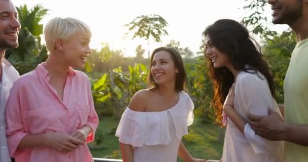 Grupo de pessoas felizes conversando ao ar livre no terraço olhando para a bela paisagem com pôr do sol sobre a floresta tropical, amigos se reunindo — Vídeo de Stock