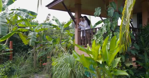 Молодая пара на балконе в тропических лесах Stnd обнимая использовать мобильный смартфон сёрфинг Интернет вместе счастливый мужчина и женщина — стоковое видео