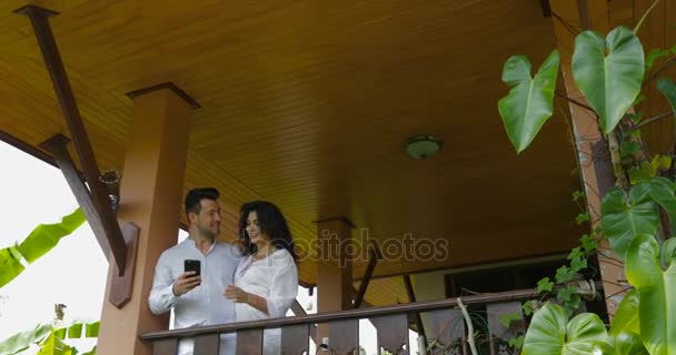 Lyckliga paret håller cellen Smart telefon chattar Online, Man och kvinna som omfamnar på balkong meddelanden Online utomhus — Stockvideo