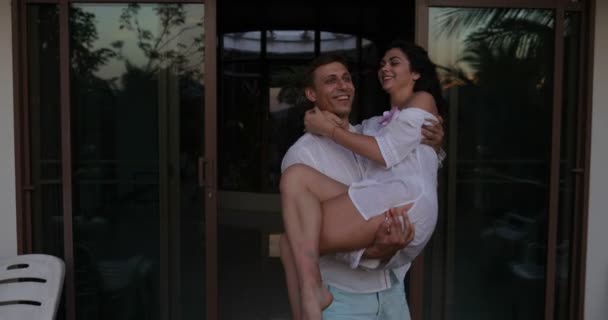 Homem feliz leva mulher para fora no terraço no por do sol, casal romântico no amor beijando sobre paisagem tropical — Vídeo de Stock