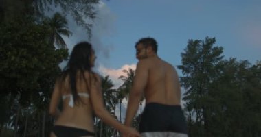 Erkek ve kadın alacakaranlıkta birlikte elele sahilde turistler iki sahil üzerinde yürüyor.