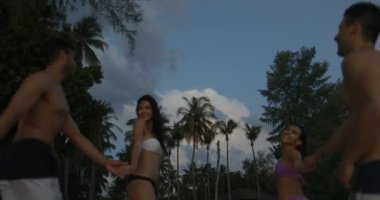 İki çiftler konuşan kumsalda güneş battıktan sonra kızlar erkekler üzerinde palmiye ağaçları önde gelen Twilights içinde yürüyüş