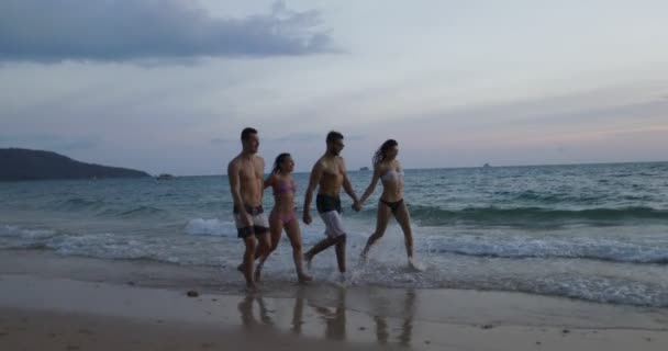 Grupo de personas caminando en la playa al atardecer, comunicación de pareja de dos razas mixtas durante las vacaciones de verano — Vídeo de stock
