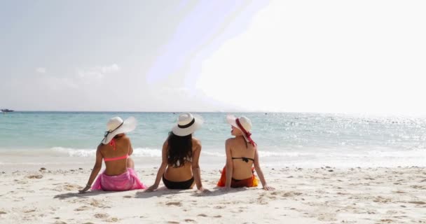 Volver Vista trasera de tres chicas en la playa en bikini, Disfrutar de bronceado hablando, Mujer quitándose sombreros de paja turistas en vacaciones de verano — Vídeos de Stock