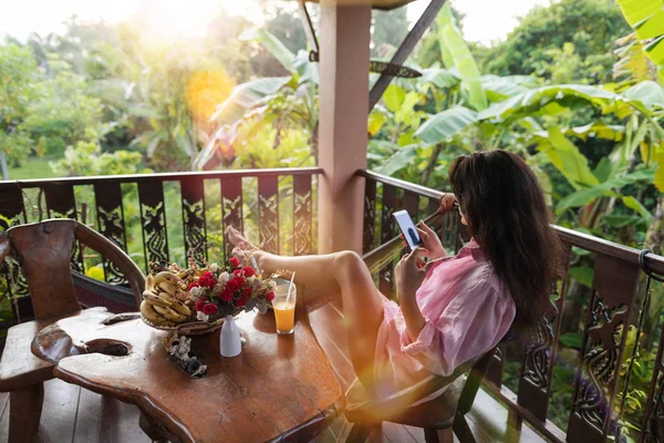 Fiatal nő gazdaság okos mobiltelefon teraszon trópusi kert hátsó hátulnézet gyönyörű lány élvező Tropic erdős táj üzenetküldés Online — Stock Fotó
