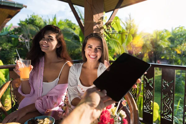 İki mutlu gülümseyen kadın alarak dijital Tablet Pc erkek eliyle birlikte yaz terasında kahvaltı ederken