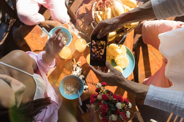 Hombre irreconocible tomando una foto de la mesa servida con frutas frescas y avena Porridge grupo de personas desayunando por la mañana — Foto de Stock