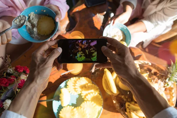 Vue d'angle supérieur des mains masculines prenant la photo de la table de petit déjeuner avec des fruits frais et de la bouillie d'avoine — Photo