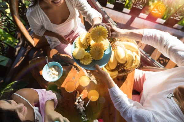 Grupo de pessoas que tomam café da manhã juntos desfrutar de abacaxi fresco jovem irreconhecível homem e mulher de manhã sentar na mesa com aveia e frutas — Fotografia de Stock