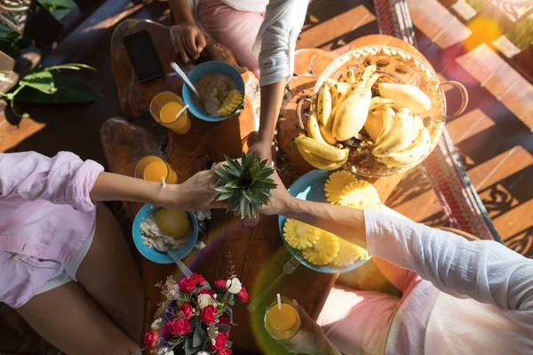 Personas sosteniendo la piña en las manos juntas en la mesa del desayuno Hombre y mujer irreconocibles por la mañana — Foto de Stock