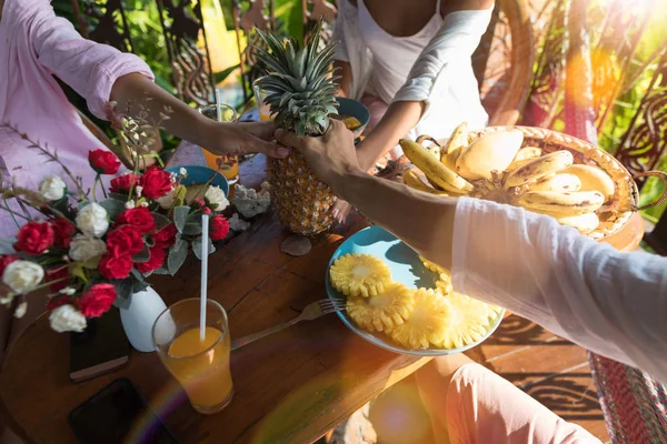 Groupe de personnes méconnaissables à la table du petit déjeuner tenant l'ananas entre les mains Jeune homme et femme le matin mangeant des fruits frais — Photo