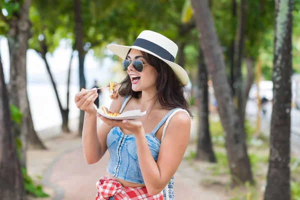 Hermosa mujer comiendo comida de la calle asiática caminando en el parque en la playa Joven turista Pruebe comida exótica durante las vacaciones — Foto de Stock