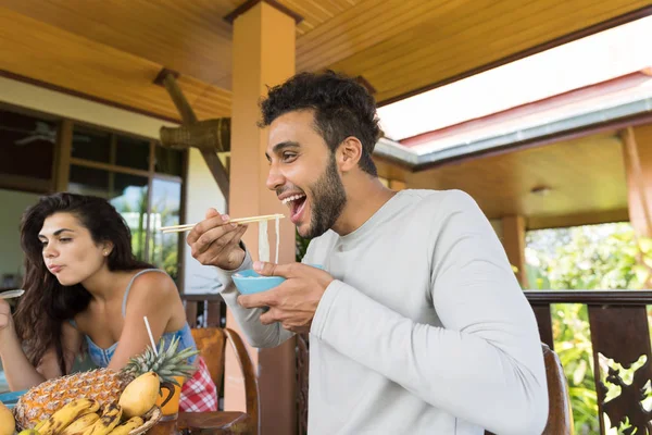 Allegro persone degustazione asiatico tagliatelle mangiare con bacchette insieme amici incontro e communicating — Foto Stock