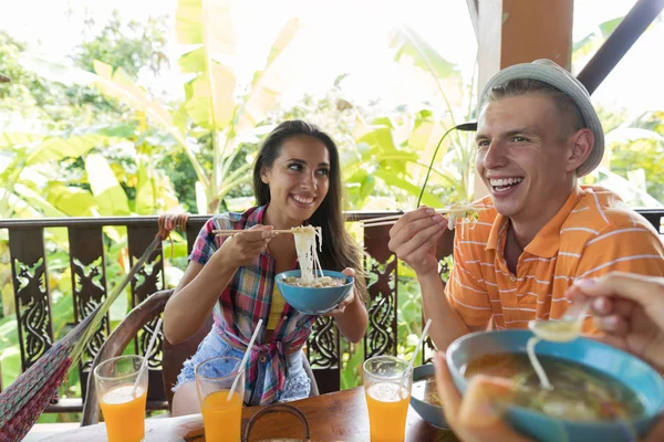 Mladí lidé jíst čínské nudle, šťastný úsměv spolu stolování na letní terase — Stock fotografie