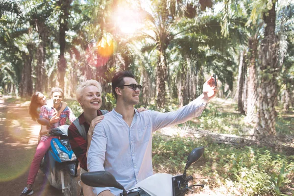 Gente felice che fa il motorino di guida di ritratto di selfie e godendo il viaggio di strada di vacanza di estate due coppie prendono la foto di auto sul viaggio dello Smart Phone delle cellule sulle bici insieme — Foto Stock