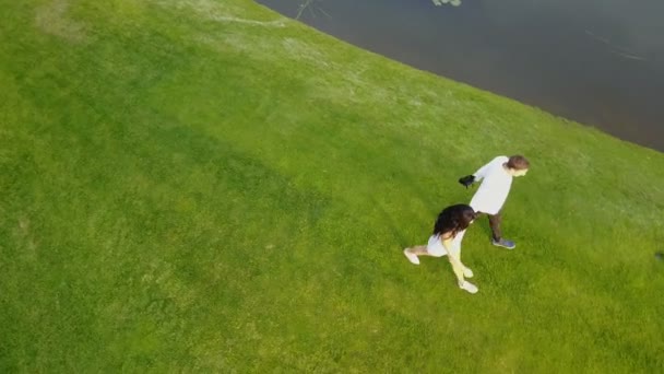 Paar läuft im Freien in der Nähe des Flusses Luftaufnahme, junger Mann und Frau halten sich Händchen in Park-Drohne schießen — Stockvideo