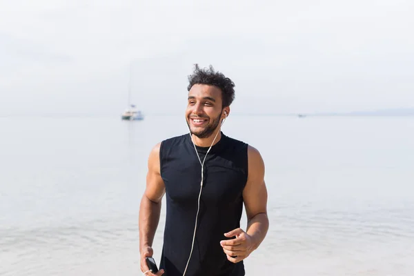 Joven corredor hispano feliz sonriendo en la playa trotando en el mar Masculino Latino Sport Fitness Training al aire libre —  Fotos de Stock