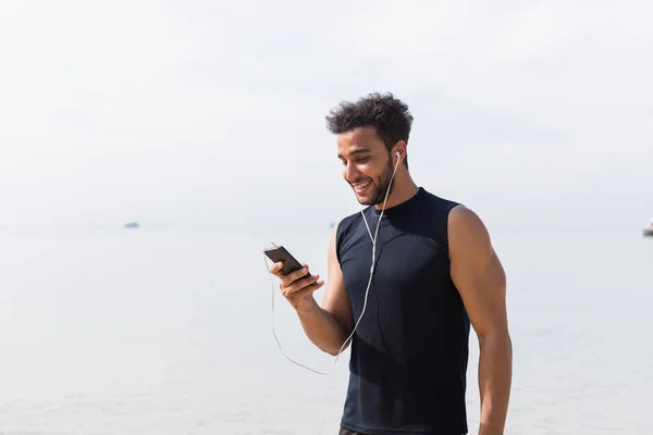 Corredor masculino hispano usando teléfono celular inteligente en la playa mientras trota en el hombre costero Joven feliz sonriente Latin Sport —  Fotos de Stock