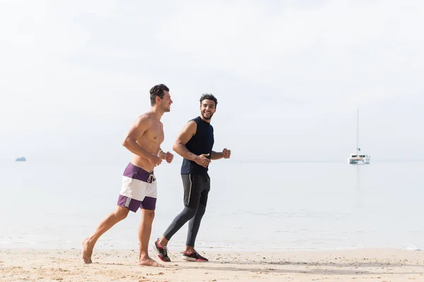 Dos hombres corriendo juntos en la playa chicos corredores entrenando en el deporte junto al mar entrenamiento de fitness al aire libre —  Fotos de Stock