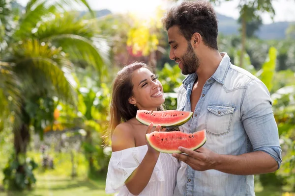 Felice coppia abbracciare guardando ogni altri tenere anguria fetta all'aperto nel parco tropicale attraente uomo e donna — Foto Stock