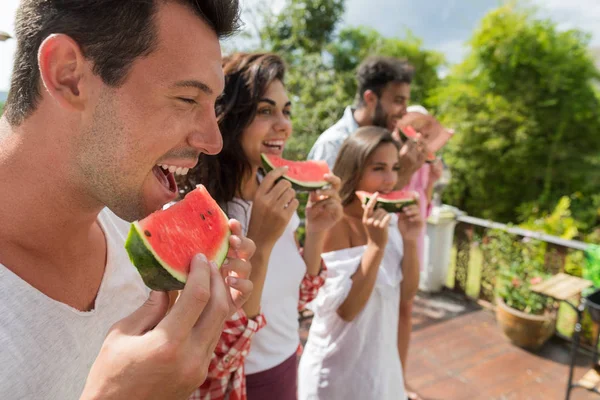 スイカ一緒に幸せな笑みを浮かべて友達の楽しい時を過すを食べている人々 の Chherful グループの側面図 — ストック写真