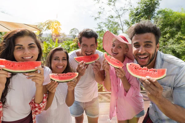 Веселий Група друзів з кавун скибочку посміхатися разом їдять воді дині на літній терасі щасливі усміхнений молодь весело — стокове фото