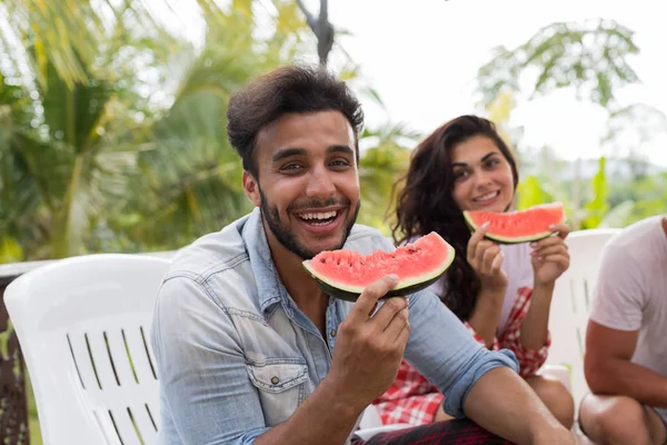 Alegre latino hombre con sandía rebanada sonrisa junto con grupo de amigos comiendo sandía juntos en verano terraza —  Fotos de Stock