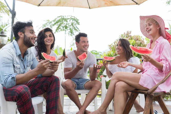 Grupo de jóvenes comiendo sandía mientras conversan juntos se divierten en la terraza de verano en el bosque tropical —  Fotos de Stock