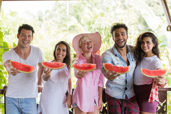 Neşeli grup arkadaşıyla birlikte eller birlikte mutlu yaz terasında gülümseyen içinde karpuz dilimi germe
