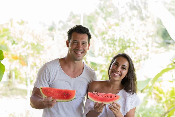 Glückliches Paar hält Wassermelonenscheibe in den Händen fröhlich lächelnd Mann und Frau umarmen sich mit Wassermelone im Freien — Stockfoto