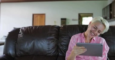 Kadın Tablet bilgisayar kullanarak gülümseyen kız Internet iletişim konuşan Koç oturma odasında oturmak Online Video çağrısı yapma veya paylaşma