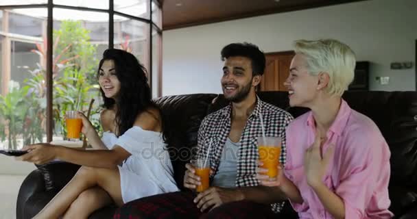Ül az edző Watch Tv, nappali lány megváltoztatása csatornák isznak gyümölcslé, fiatal férfi és nő csoport reggel beszél a Modern apartman — Stock videók