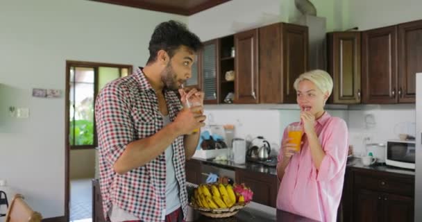 Casal na cozinha beber suco de laranja de manhã, jovem e mulher falando café da manhã — Vídeo de Stock