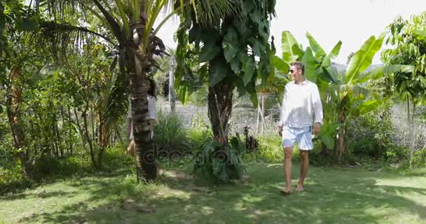 男性と女性の屋外手話、幸せを繋いでいるトロピカル ガーデンで歩くカップル — ストック動画