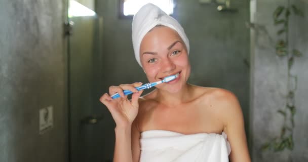 Mujer cepillando los dientes en el baño, alegre hermosa chica en toalla feliz sonrisa haciendo higiene de la mañana — Vídeos de Stock