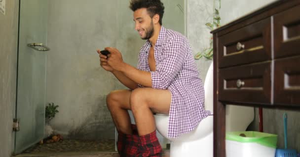 男のトイレに座って使用携帯スマート フォン若いラテン男ゲームをプレイ — ストック動画