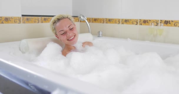 Banho jovem mulher relaxante no banho cheio de espuma levantando pernas, sorrindo menina bonita goza de spa em casa — Vídeo de Stock