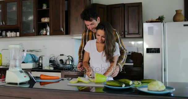 L'homme embrasse la femme coupant des légumes pour préparer un dîner sain parlant couple dans la cuisine cuisiner ensemble — Video