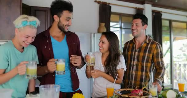 Twee koppels praten In keuken proeven van vers sap, de jonge Man en de vrouw drinken samen gelukkig lachend — Stockvideo