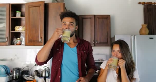 Paar trinkt frischen Smoothie plaudernd Mann und Frau in Küche zusammen glücklich lächelnd — Stockvideo